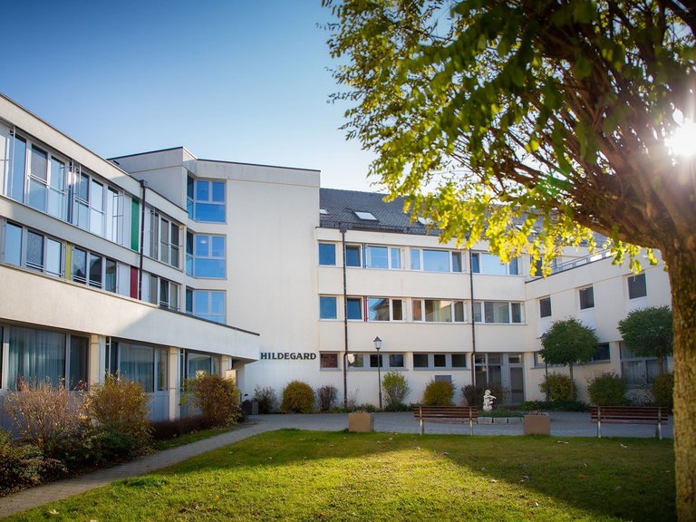 Das Altenheim St. Hildegard von außen mit strahlend blauem Himmel und einem grünen Baum im Vordergrund